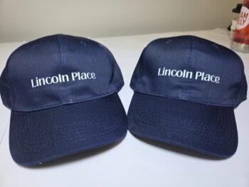 Two navy blue caps with Lincoln Place written on the front, placed side by side on a table.