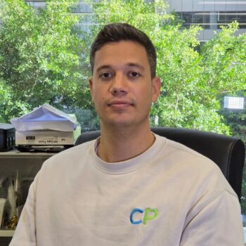 Meet the team: Man in a white CP sweatshirt sits at a desk with greenery visible behind him.