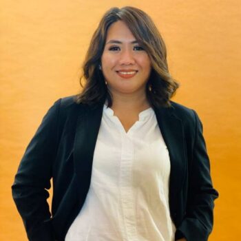 Meet the team: A woman in a black blazer and white shirt smiles against an orange background.