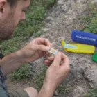 Outdoors, a man opens a Pocket Care Kit Gifts near colorful cases, one labeled YOUR LOGO HERE.