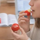 Woman applies Lip Balm Ball Branded Gifts; notebook in background, ideal for promotions.