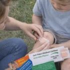 An adult applies Plaster Sleeves to a child's scraped knee outside.