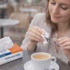 Woman at cafe cleaning glasses with tissue from Personalised Pocket Tissue Boxes over coffee.
