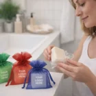 Woman unwraps Organza Soap Bar Printed Gifts; colorful boxes show Your Logo Here on counter.