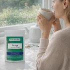 A woman drinks tea by a window with Herbal Tea Packs on the counter beside her.