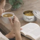 Woman drinks tea and reads, with Herbal Tea Tins on the table.