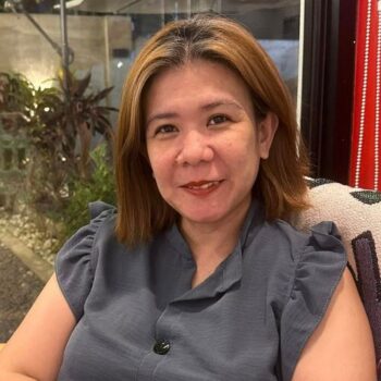 Meet the team: A woman with shoulder-length hair smiles indoors, wearing a gray blouse.