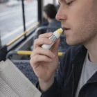 Man on a bus holding customised zinc face paint sticks, applying lip balm and reading.