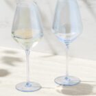 Two wine glasses on a light surface, one filled with white wine, one empty.
