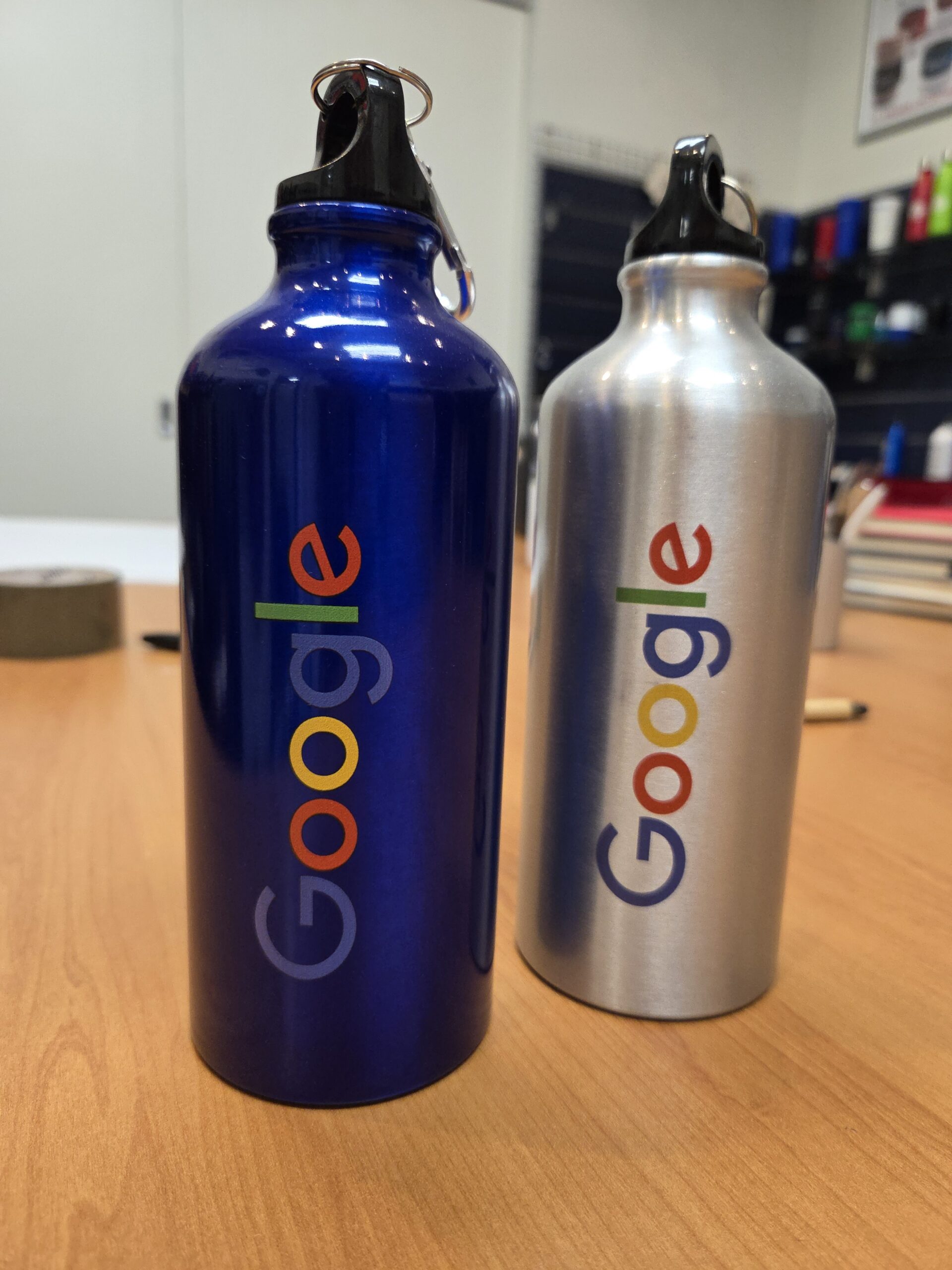 Two Google-branded water bottles showcasing branding methods on a wooden table.