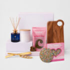 Gift set with candle, diffuser, chocolates, cheese knife, and wooden serving board.