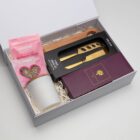 Gift box with chocolates, cheese knives, a wooden board, and a white candle.