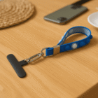 A blue wrist strap keychain with a T-shaped black object on a wooden table.