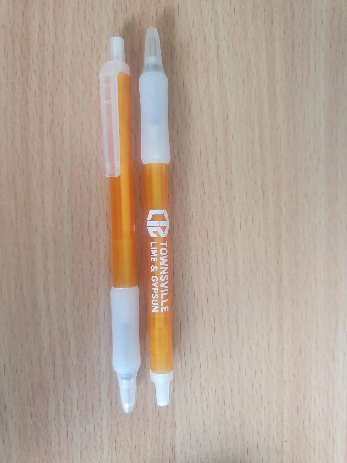 Two orange and white pens—great universal event gifts—on a light wooden surface.
