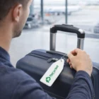 Man holding a suitcase with an Olyx Vinyl Key Tag at the airport terminal.
