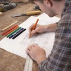 Person drawing plans with Printable Carpenters Pencils and ruler on a wooden worktable.