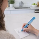 Someone writes a grocery list in the kitchen using a Lodestone House Fridge Pen.