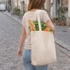Woman carries Gobags Cotton Tote Bags with bread, carrots, and greens on a cobblestone street.