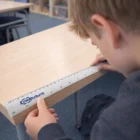 A boy uses a 30Cm Custom Metal Ruler to measure a desk's edge in class.
