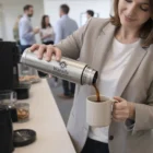 Woman pours coffee from a 750Ml Event Vacuum Flask into a mug in an office break room.