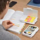 Person marking passages in an open book with Flicknotes Flag Pads on a desk.