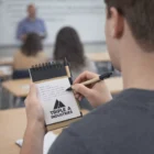 Student taking notes with an Inked Notebooks notepad labeled TRIPLE A INDUSTRIES.