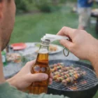 Opening a beer with Dukie Bottle Opener Keychains by the grill and skewers.