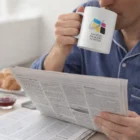 Person in pajamas enjoys coffee from Cuppa Coffee Mugs while reading the morning newspaper.