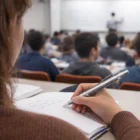 A student writes notes with Tictac Pens as a teacher writes on the board in class.