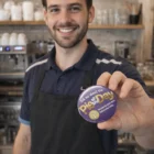 Smiling barista holds a Fintex Button Badges Round 75mm in a café.