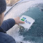 Person scraping frost from a car window with a Glacia Ice Scraper on a winter day.