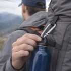 Attaching a blue water bottle to a gray backpack with Jaxon Carabiners outdoors.