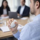 Man holding a Rugby Stress Ball Shapes in a meeting with two colleagues in a conference room.