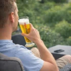 Man relaxing outdoors with a Tall Emblazoned Beer Glass, greenery in the background.