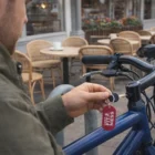 Man locks blue bike with Odeo Key Ring near outdoor café tables.