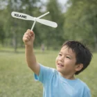 Smiling boy in blue shirt holds a Kids Toy Spins Copter outdoors in a green park.