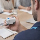Man holding a Blox Van Stress Ball labeled TrackNet during a meeting with notebooks on table.