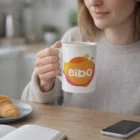 Woman enjoying breakfast with a Bone China Premium Mug featuring a colorful eibo logo.