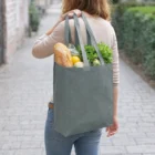 Woman carries groceries in Eco Lovati Tote Bags, filled with bread and veggies, walking outside.