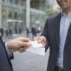 Two men in suits exchange Single Card Holder Keyrings outside an office building.