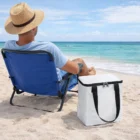 Man in a hat relaxes by the ocean with The Coolio Cooler Bags beside his beach chair.