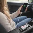 Person powers phone in car's cup holder using Enero Mini Car Chargers.