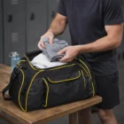 Packing gym clothes into a Nelly Duffle Bag with yellow trim on a wooden table.