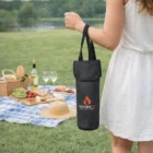 Woman by a lake holding an Amora Wine Cooler Bag near a picnic setup with wine accessories.
