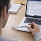 Person holding a Vistra 4Gb Flash Drive Pen near a laptop, notebook, and document.