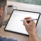 Person sketching on a tablet with a Broome Stylus Pen beside coffee on a wooden table.