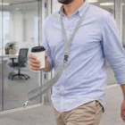 Man in light blue shirt with coffee cup, wearing a gray Ollen Lanyards lanyard at the office.