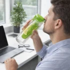 Man uses Fruit Infuser Water Bottle at desk with laptop and glasses.