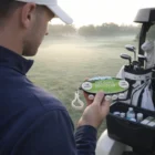 Man holding Golf Tee Holders by a golf cart on a misty course.