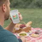 Man holding a Budget Reusable Event Cup at a picnic with sandwiches, fruit, and a basket.